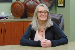Woman seated at desk with pottery background.